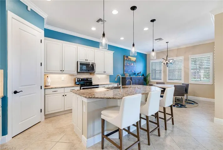 Kitchen featuring tasteful backsplash, light stone countertops, pendant lighting, ornamental molding, and appliances with stainless steel finishes