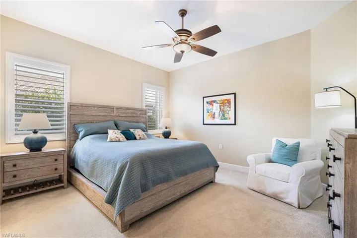Primary Bedroom with two windows with plantation shutters, neutral color scheme, ceiling fan.