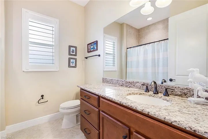 Full guest bath with vanity, light tile patterned floors, curtained shower and plantation shuters