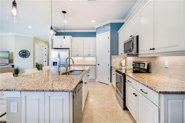 Kitchen with stainless steel appliances, a kitchen island with sink, ornamental molding, light stone counters, and tasteful backsplash