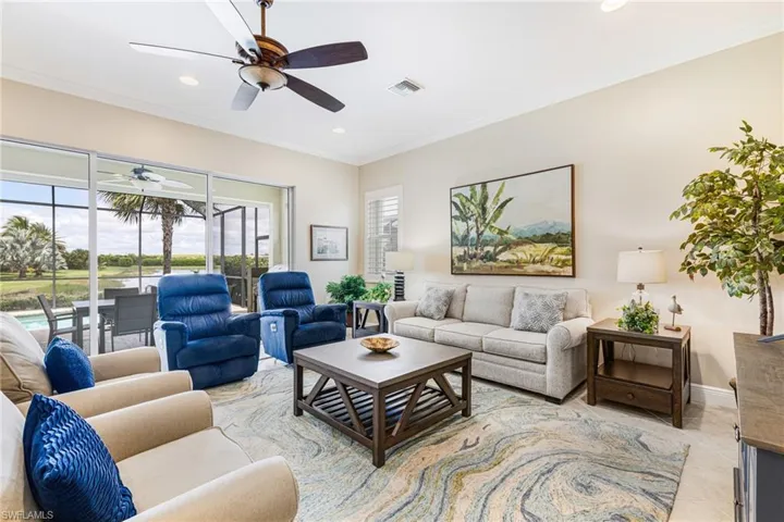 Great room looking out through stacking sliding doors onto Lanai and Lake. Features crown molding, recessed lighting, light tile patterned floors, and a ceiling fan
