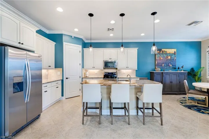 Kitchen with appliances with stainless steel finishes, light stone countertops, decorative backsplash, decorative light fixtures, and crown molding