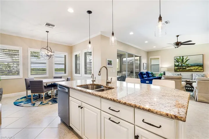 Kitchen featuring white cabinetry, pendant light fixtures, light stone counters and a kitchen island with sink