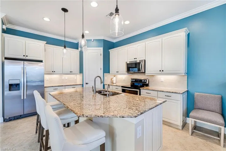 Kitchen featuring stainless steel appliances, backsplash, a kitchen island, light stone countertops, white cabinetry with under cabinet lighting and ornamental molding