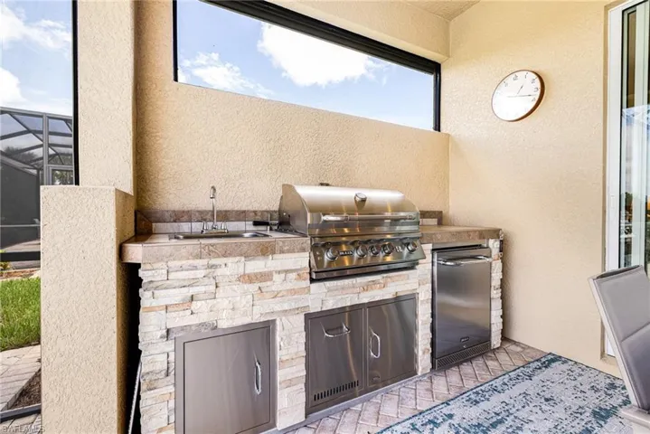 View of lanai featuring an outdoor kitchen with sink, grill and refrigerator.