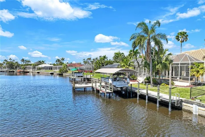 Dock area featuring glass enclosure, a lawn, a water view, and boat lift