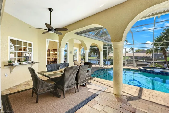 View of pool with glass enclosure, a ceiling fan, outdoor dining area, a pool with connected hot tub, and a patio area