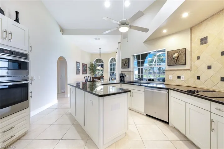 Kitchen with a sink, backsplash, arched walkways, appliances with stainless steel finishes, and ceiling fan