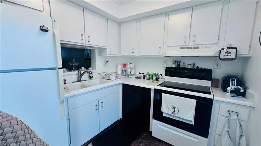Kitchen with freestanding refrigerator, range with electric cooktop, under cabinet range hood, light countertops, and white cabinets