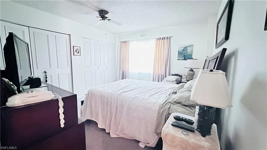 Carpeted bedroom featuring multiple closets, ceiling fan, and a textured ceiling