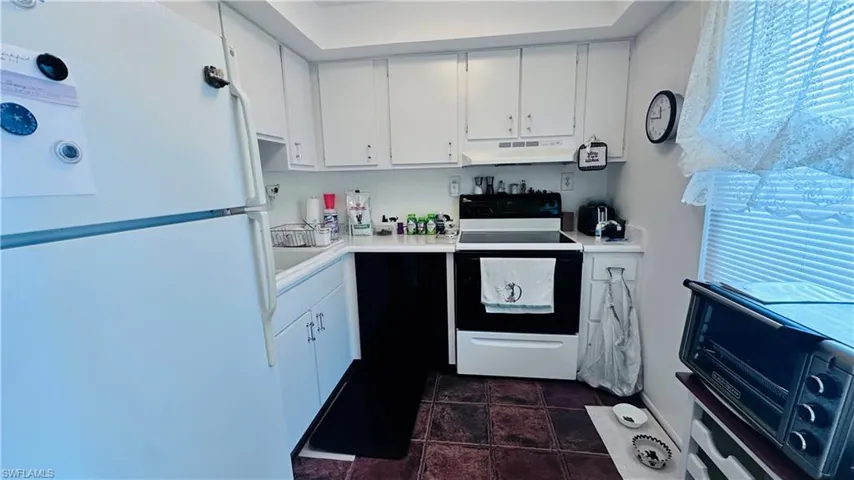 Kitchen with freestanding refrigerator, electric range, under cabinet range hood, white cabinets, and light countertops