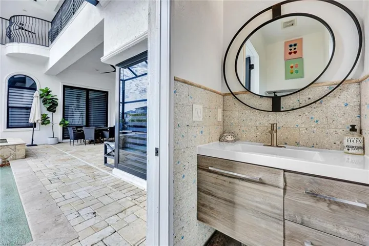 Floating vanity with wood-finish cabinetry, rectangular vessel sink, metallic faucet, decorative tile backsplash, and oversized oval wall mirror