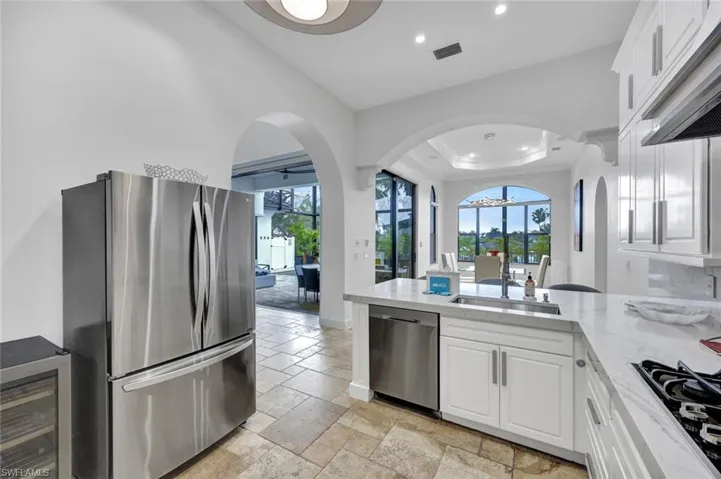 Kitchen featuring stainless steel appliances, white cabinetry, stone-finish countertops, tile flooring, and arched architectural entryways