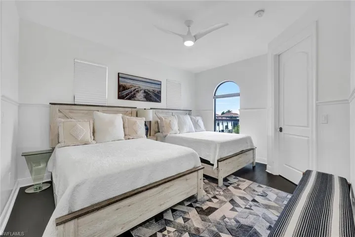 Bedroom featuring dark wood-finish flooring, white wainscoting, a ceiling fan, and an arched window
