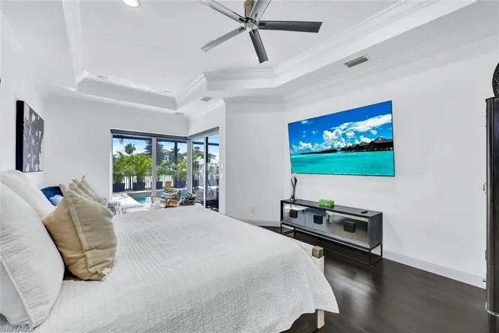 Tray ceiling with crown molding, dark wood-finish flooring, recessed lighting, and a modern ceiling fan, featuring sliding glass doors providing outdoor access