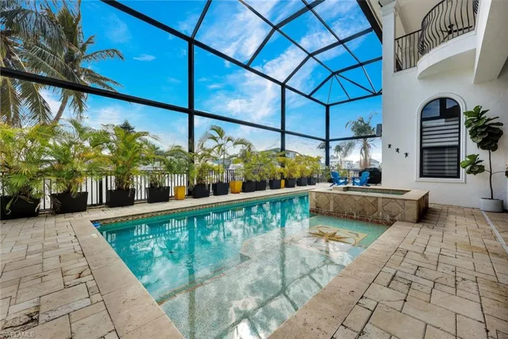 Screened lanai featuring a rectangular swimming pool with integrated spillover spa, decorative tile inlay, stone pool deck, and black metal framing