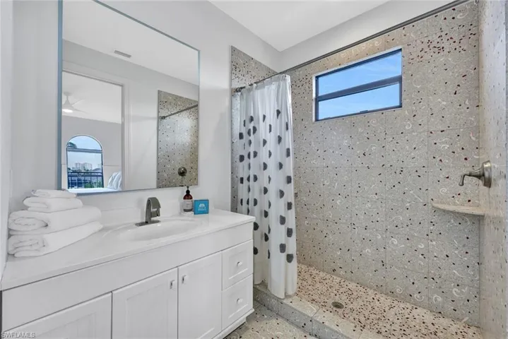 Bathroom vanity with a white countertop, integrated oval sink, and single-handle faucet, featuring a large wall-mounted mirror and a walk-in shower with terrazzo-style tile and built-in corner shelving