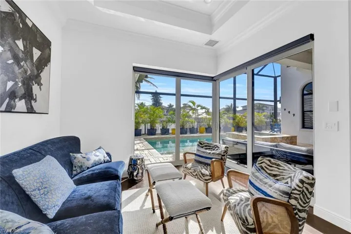 Tray ceiling with recessed lighting, expansive multi-panel sliding glass doors, and direct access to an enclosed pool and stone-paved patio