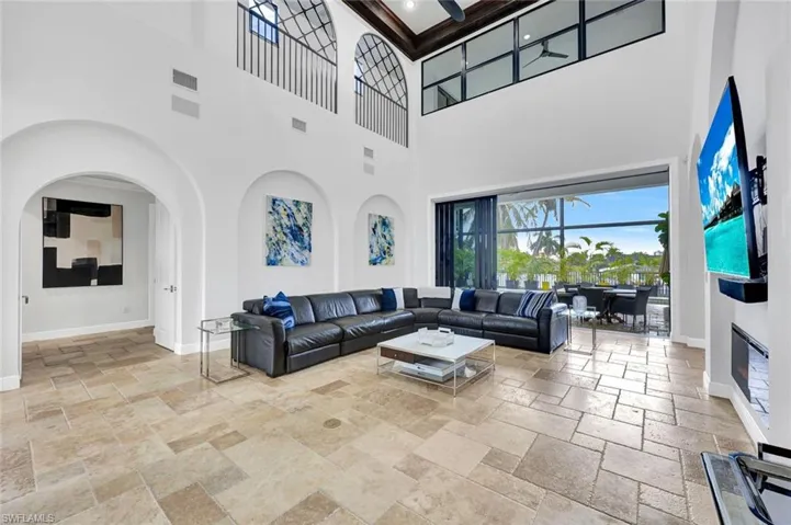 Double-height living area featuring coffered wood-beam ceilings, arched wall niches, decorative iron railings on an upper gallery, and large-format stone-tile flooring