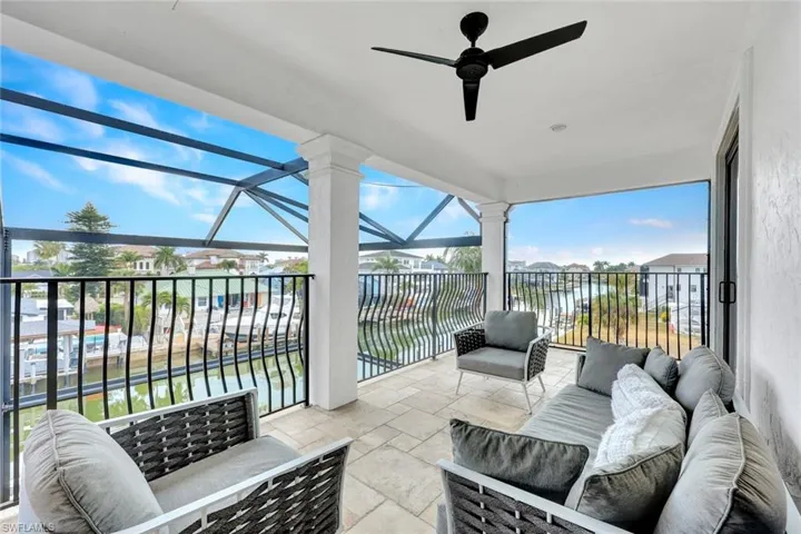 Covered balcony featuring stone-finish flooring, black metal railing, and a mounted ceiling fan