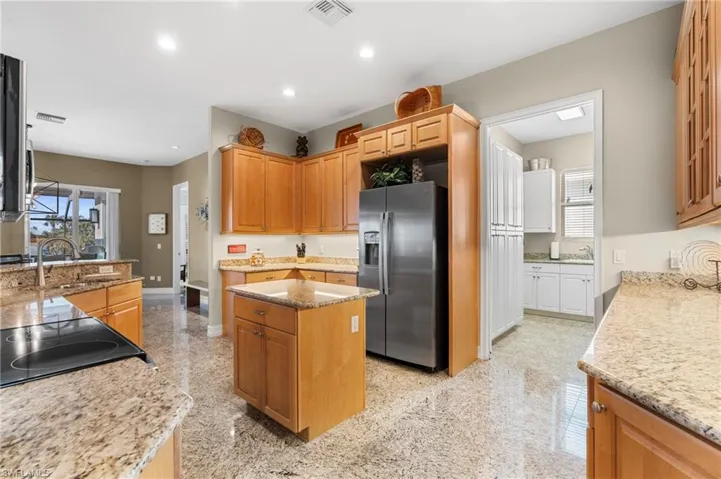 Kitchen featuring light stone counters, sink, stainless steel fridge, and a center island