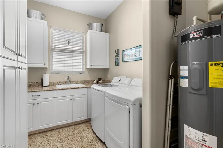 Clothes washing area with separate washer and dryer, sink, cabinets, and electric water heater
