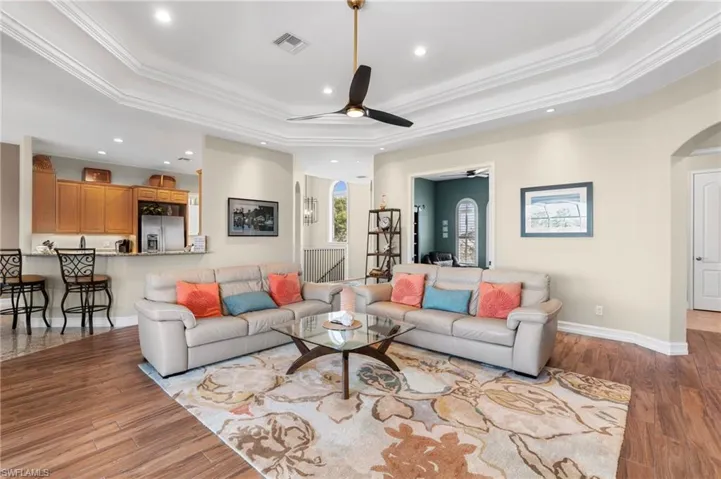 Living room with ceiling fan, ornamental molding, a raised ceiling, and light hardwood / wood-style floors
