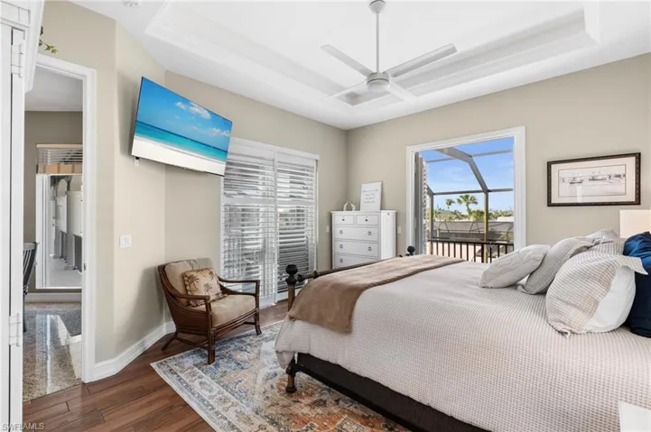 Bedroom featuring dark wood-type flooring, ceiling fan, a tray ceiling, and access to outside
