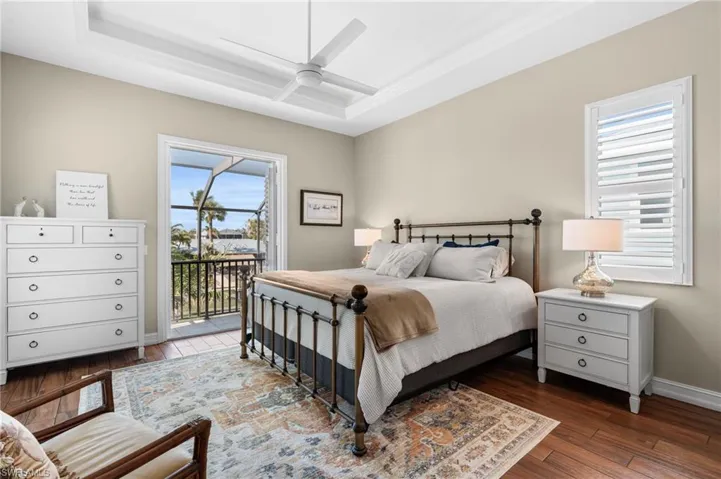 Bedroom featuring dark wood-type flooring, ceiling fan, a tray ceiling, and access to exterior