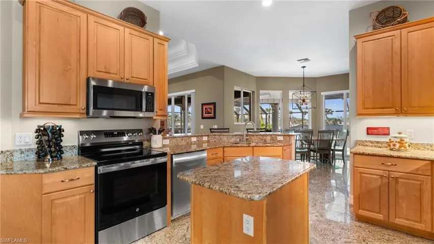 Kitchen with pendant lighting, light stone countertops, an island with sink, and appliances with stainless steel finishes