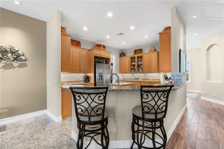 Kitchen with a kitchen breakfast bar, dark stone counters, kitchen peninsula, and stainless steel refrigerator with ice dispenser