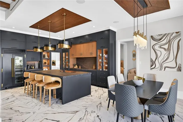 Kitchen with dark countertops, a kitchen breakfast bar, a large island with sink, decorative light fixtures, and built in fridge