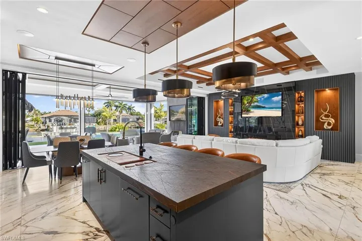 Kitchen featuring decorative light fixtures, an island with sink, coffered ceiling, open floor plan, and wooden counters