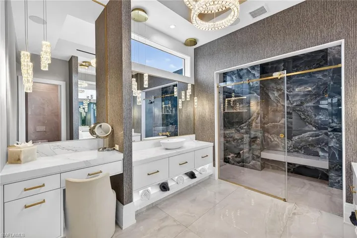 Full bath featuring vanity, a marble finish shower, light marble finish floors, and suspended lighting