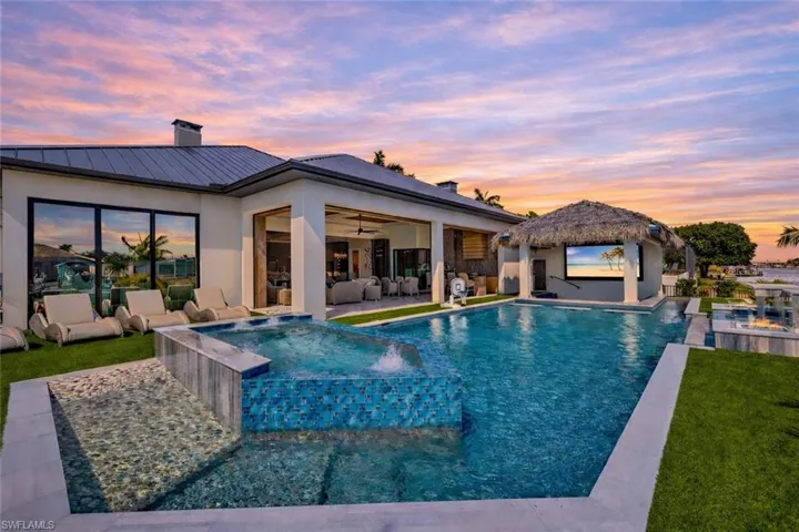 Pool at dusk featuring a pool with connected hot tub, an outdoor hangout area, a patio area, and a yard