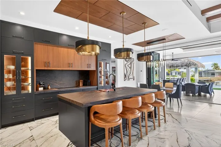 Two tone kitchen featuring dark countertops, hanging light fixtures, a center island with sink, a breakfast bar, and two tone cabinetry