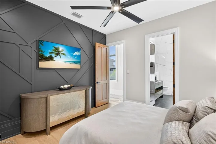 Bedroom with an accent wall, a ceiling fan, connected bathroom, and light wood-type flooring