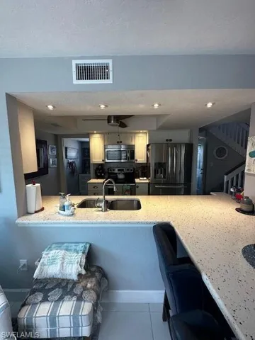 Kitchen with fridge, a peninsula, stove, stainless steel microwave, and a textured ceiling