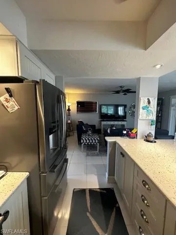 Kitchen featuring stainless steel fridge, light stone countertops, open floor plan, and light tile patterned flooring