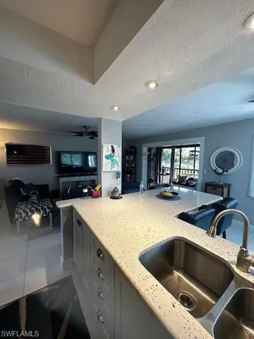 Kitchen with light stone counters, open floor plan, light tile patterned flooring, a ceiling fan, and a textured ceiling