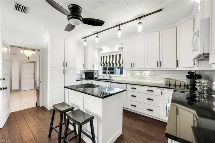 Kitchen featuring white cabinetry, a kitchen island, white microwave, dark wood-style flooring, and a kitchen breakfast bar