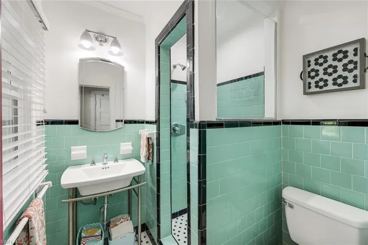 Bathroom with a stall shower, tile walls, crown molding, and a wainscoted wall