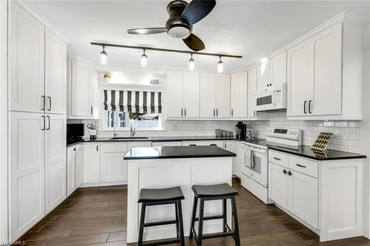 Kitchen with white appliances, a kitchen island, white cabinets, a ceiling fan, and track lighting