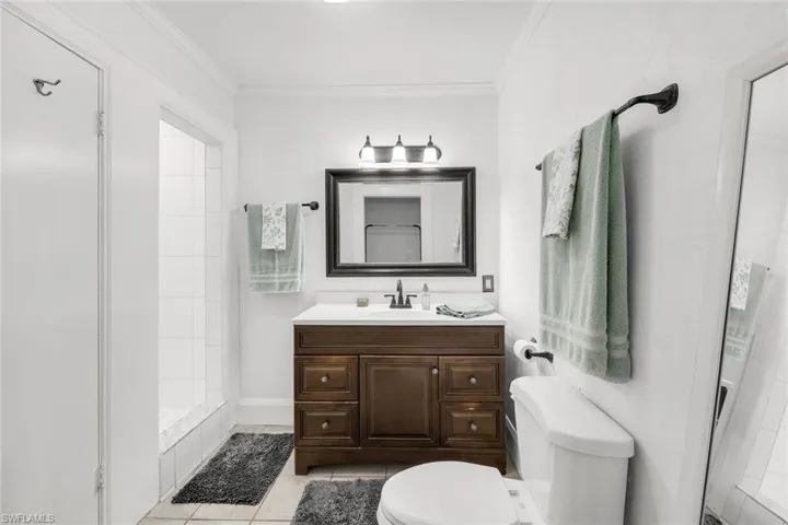 Bathroom with vanity, a tile shower, crown molding, and light tile patterned flooring