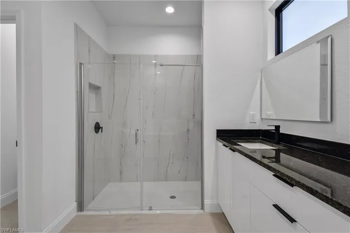 Full bath featuring a marble finish shower, light wood finished floors, and vanity