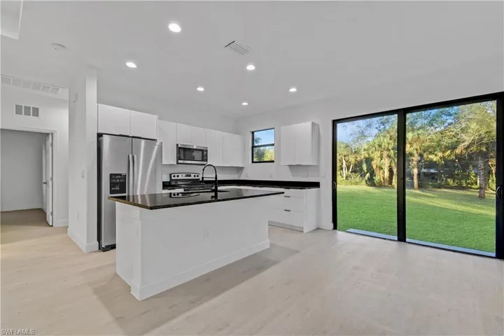 Kitchen featuring stainless steel appliances, recessed lighting, white cabinets, an island with sink, and dark stone countertops
