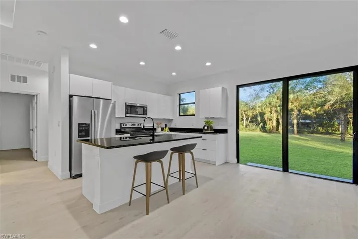 Kitchen featuring appliances with stainless steel finishes, a kitchen bar, white cabinetry, recessed lighting, and a center island with sink