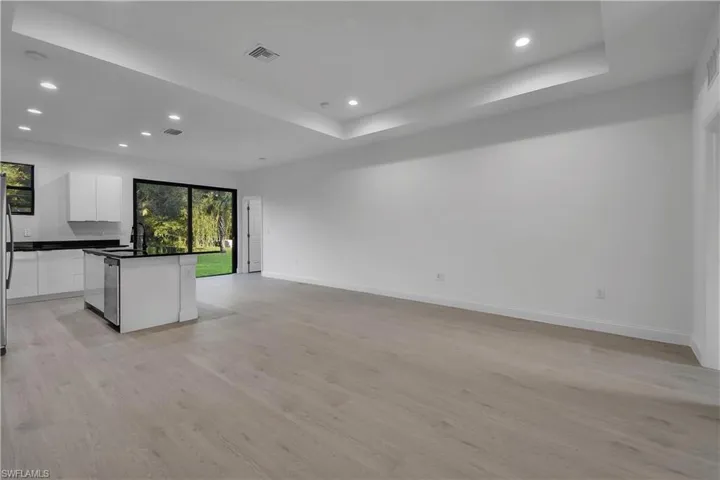 Kitchen with white cabinets, open floor plan, recessed lighting, light wood finished floors, and a tray ceiling