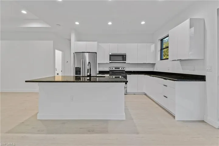 Kitchen featuring white cabinetry, appliances with stainless steel finishes, dark stone counters, recessed lighting, and an island with sink
