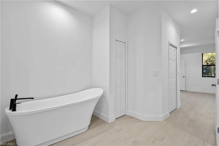 Bathroom featuring a closet, a freestanding tub, recessed lighting, and light wood finished floors